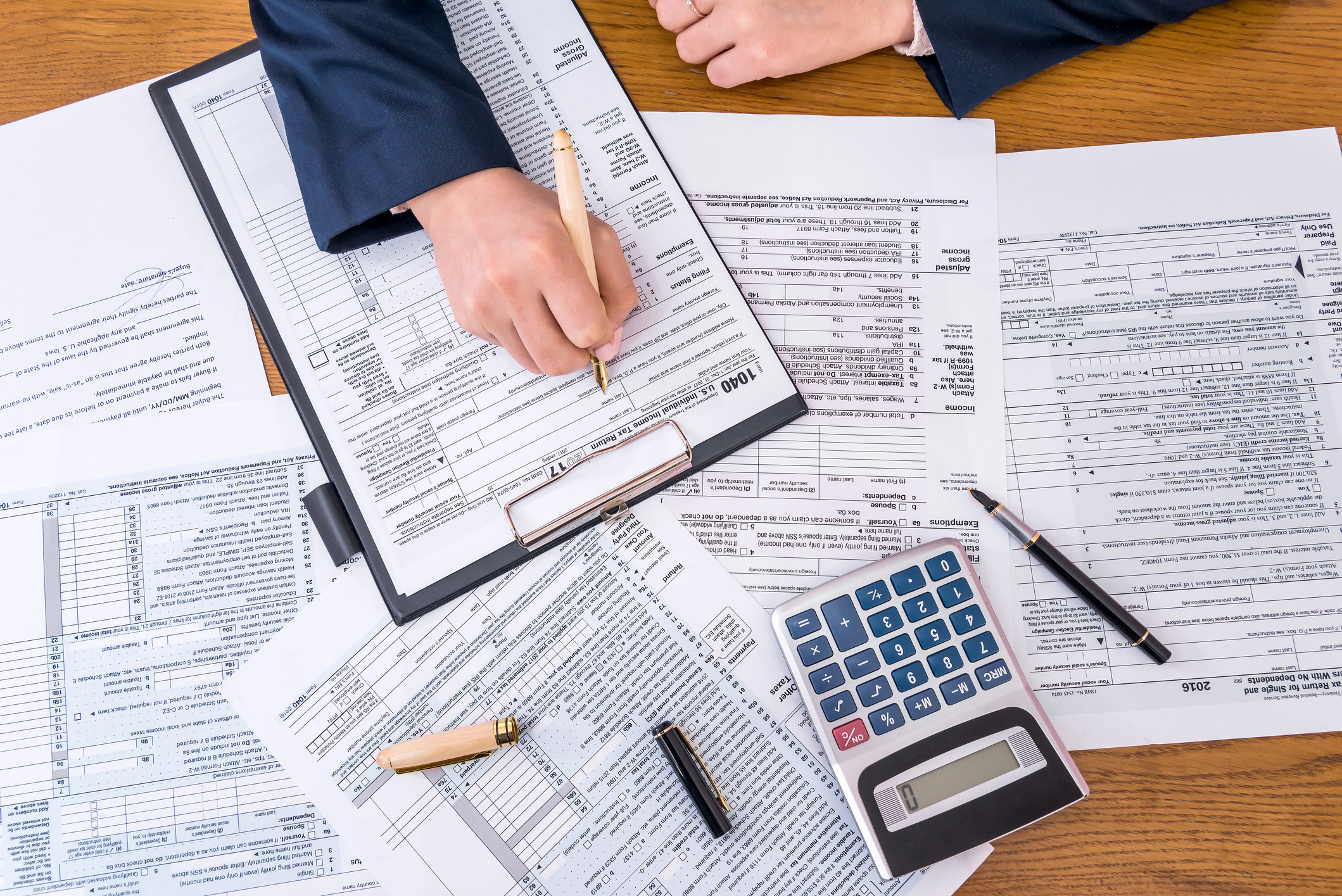 A top-down view of a desk covered in tax paperwork and a hand filling them out next to a calculator.