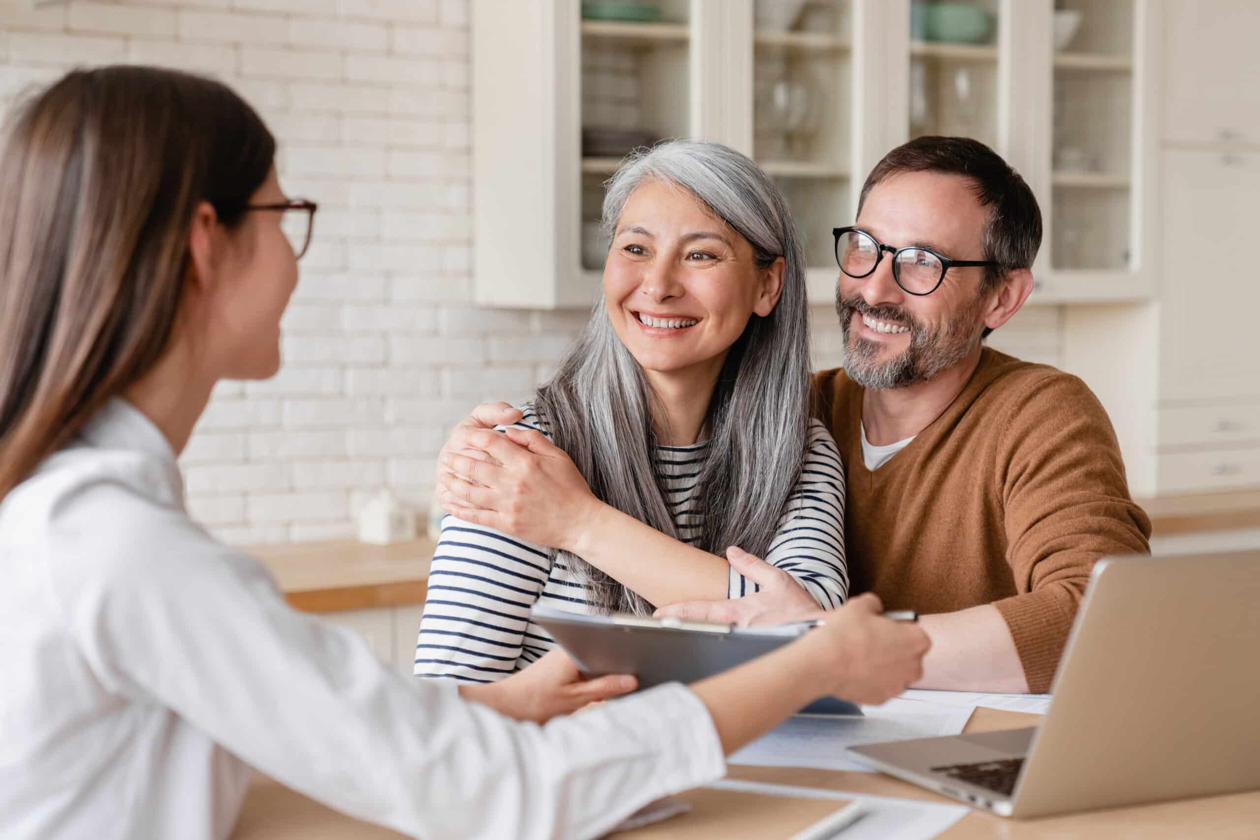 A financial advisor helping consulting showing documents on an iPadto a mature middle-aged couple at home.