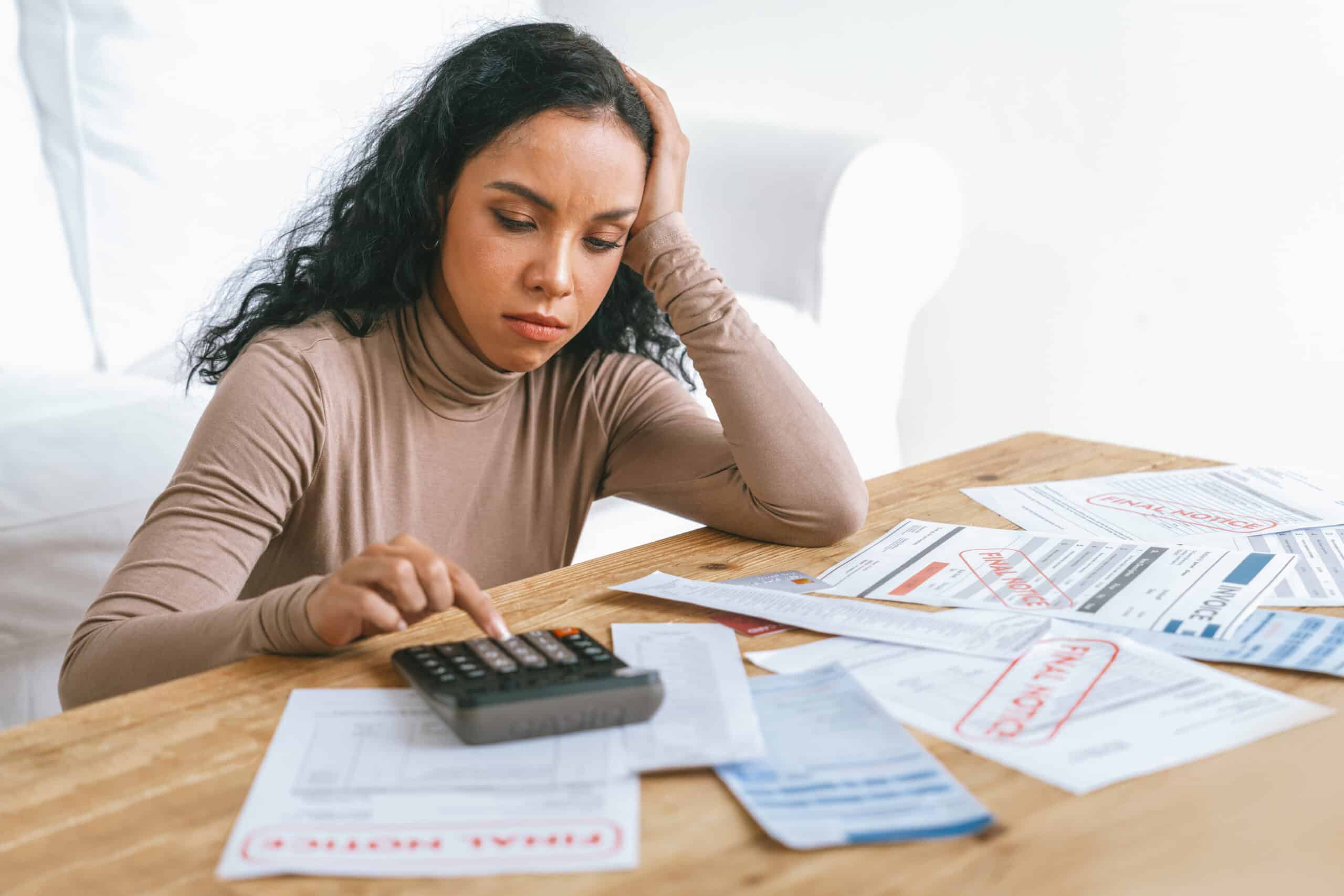 A young woman appears stressed over financial documents and a calculator.